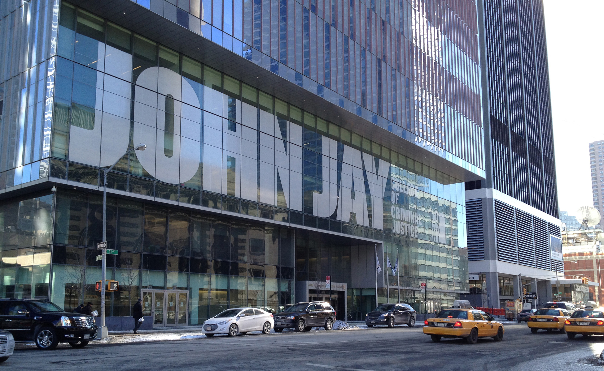 Large glass exterior sign displaying 'John Jay College' facing 9th Avenue with contemporary design